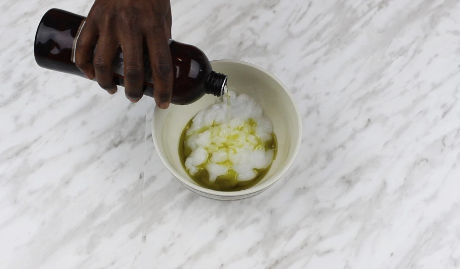 Hand pouring oil into a bowl to create DIY detangling hair mix for 4c hair